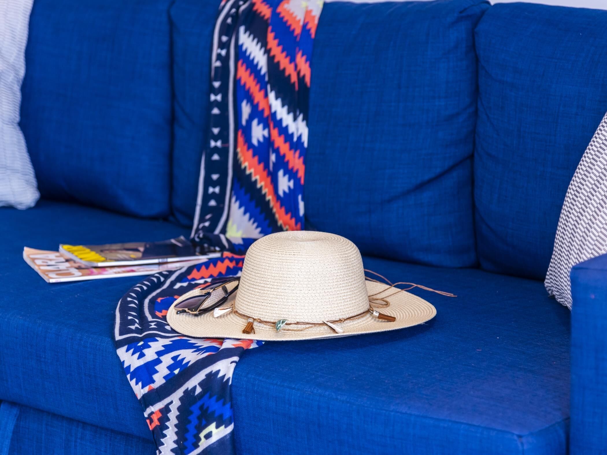A blue sofa with a woven hat and sunglasses on it.