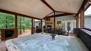 Un jacuzzi en una terraza de madera con chimenea de piedra y mobiliario exterior.