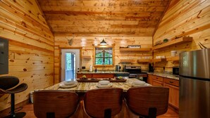 Interior de una cabaña de madera con comedor, cocina y un amplio ventanal.