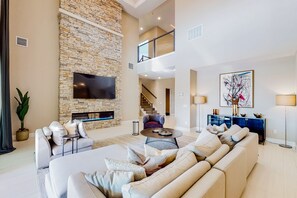 Un salón amplio con chimenea de piedra, un televisor de pantalla plana grande, un conjunto de sofás y una escalera que conduce a un nivel superior.