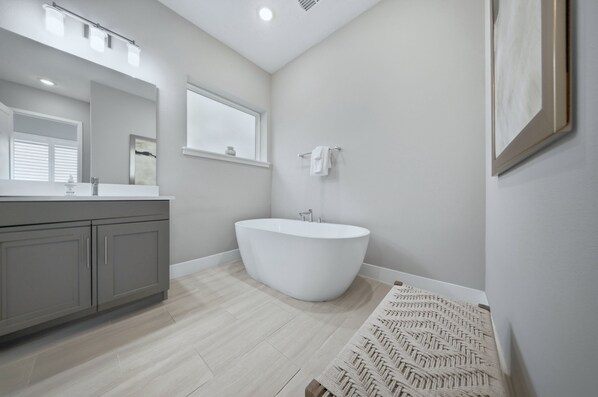 A modern bathroom with a freestanding bathtub, a large mirror, and a window.