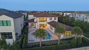 Una casa de dos pisos con piscina, mobiliario exterior y patio cercado.