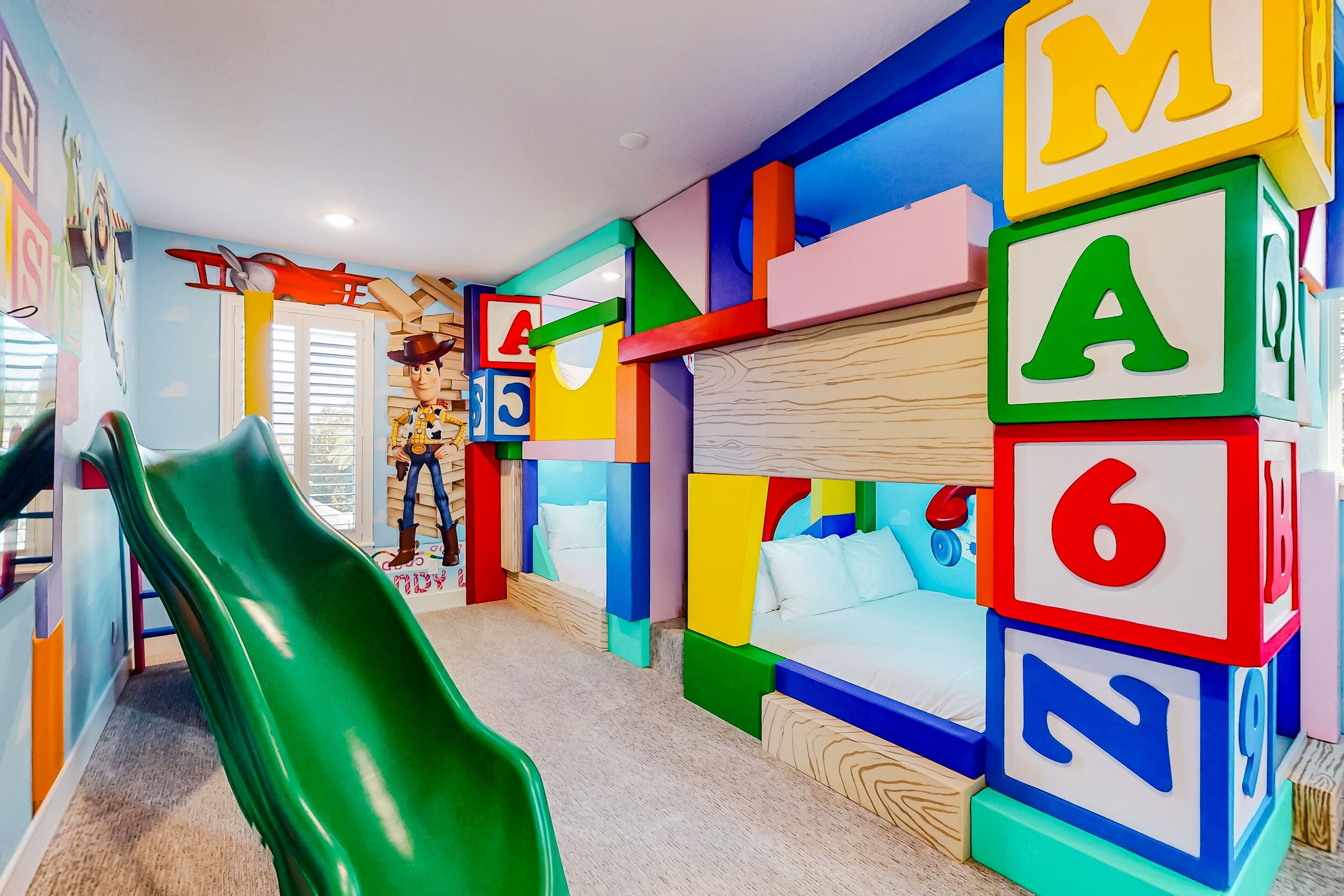 A children's playroom with a green slide, colorful alphabet blocks, and a bed with a wooden headboard.