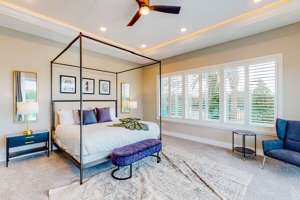 Un dormitorio con cama con dosel, ventilador de techo y ventana grande con persianas.