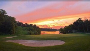 Un terrain de golf au coucher du soleil, avec une étendue d’eau en arrière-plan.