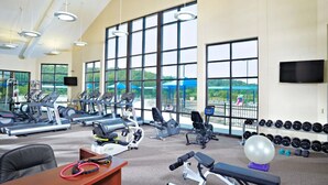 Une salle de sport équipée de machines de cardio, de matériel de musculation et de grandes fenêtres donnant sur l’extérieur.
