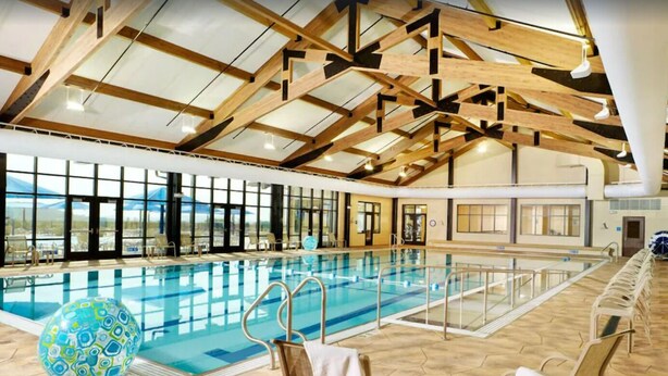 Une piscine intérieure dotée d’un haut plafond et de grandes fenêtres, entourée de chaises longues et agrémentée d’une sphère décorative.