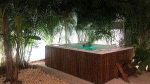 Ein hölzernes Whirlpool-Becken, umgeben von Palmen und Kieselsteinen.