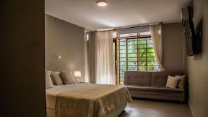 Ein Schlafzimmer mit Bett, einer Couch, einem Fenster mit Vorhängen und einem Fernseher an der Wand.