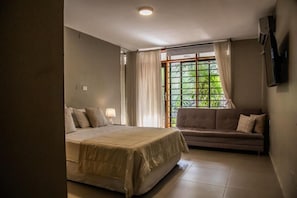 Quarto com cama, sofá, janela com cortinas e televisão na parede.