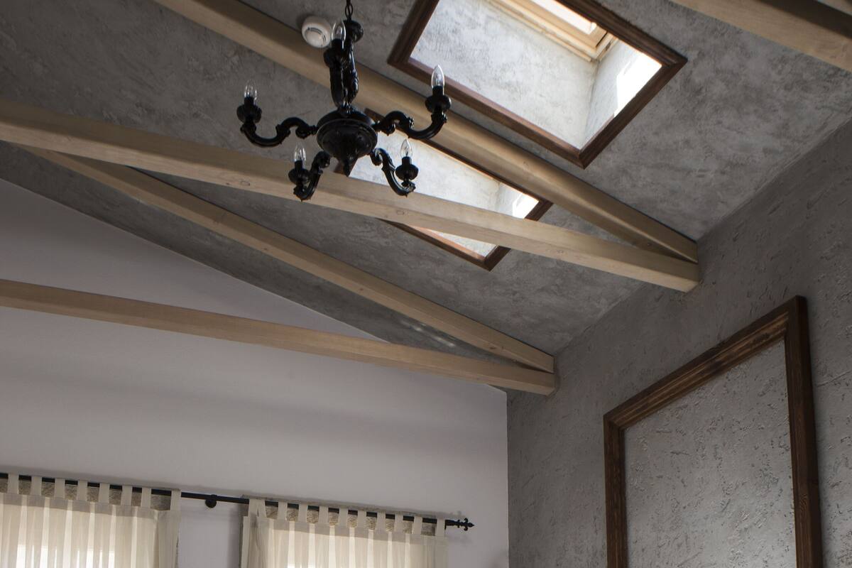 A bedroom with a bed, skylight, curtains, and a chandelier.