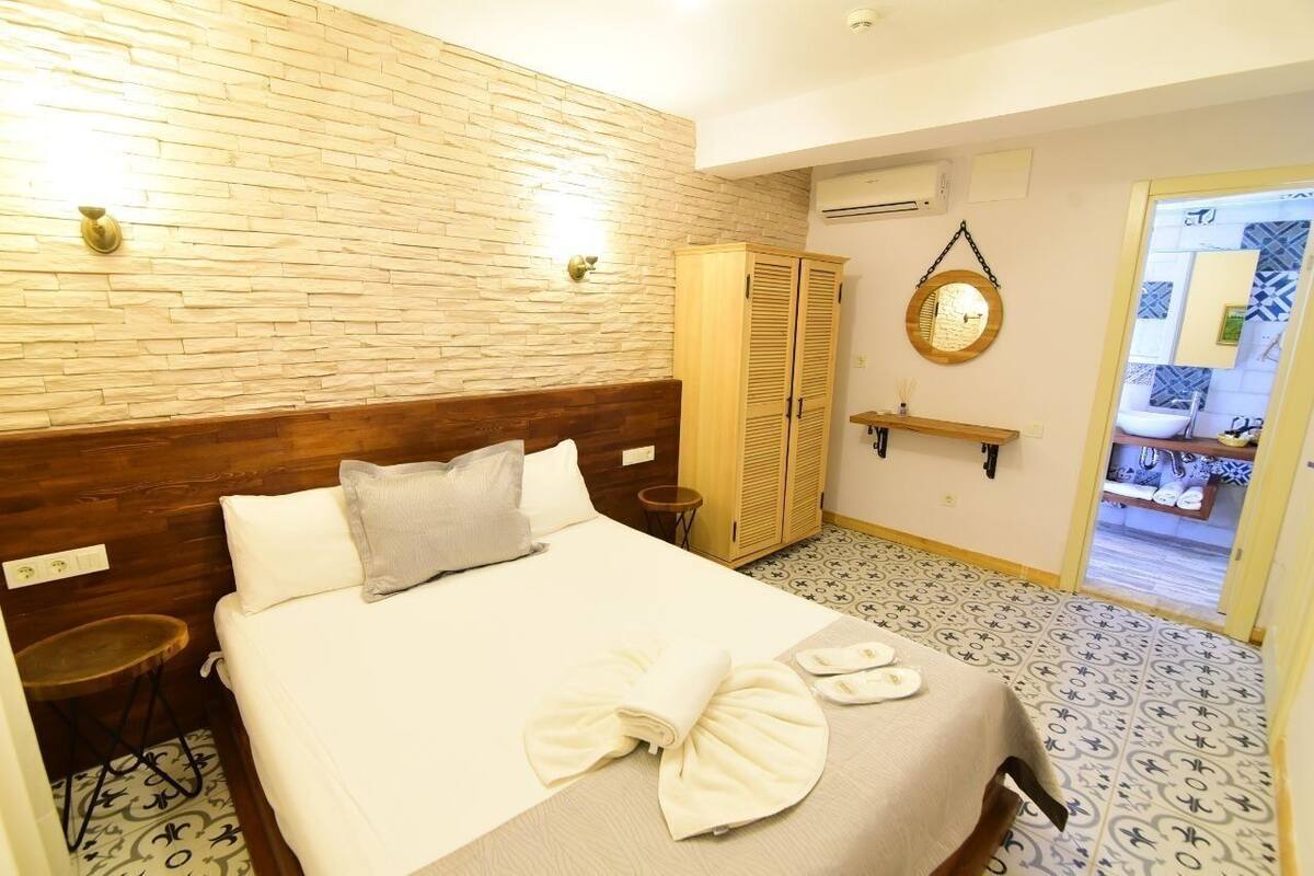 A hotel room with a wooden headboard, a bed with white linens, a small round table, a wardrobe, and a bathroom visible through an open door.