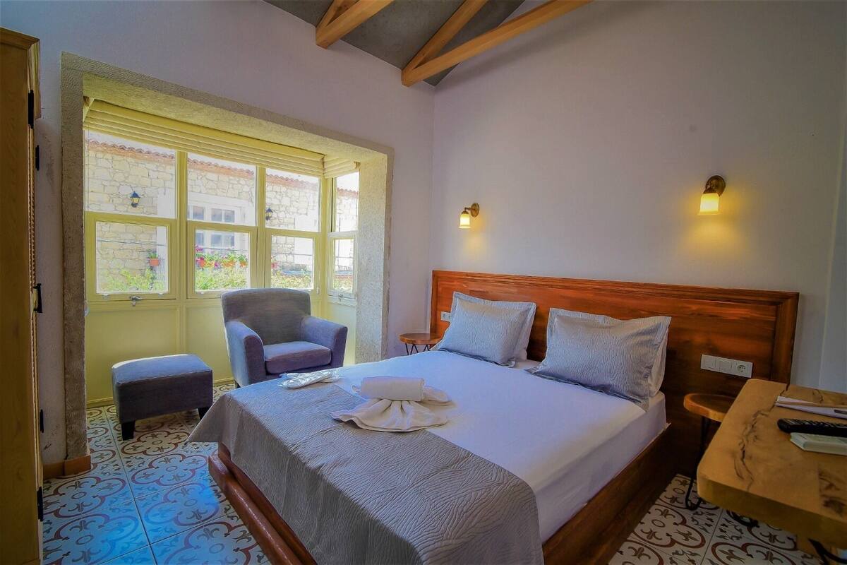 A hotel room with a large bed, a chair, a small table, and a window with a view of the outside.