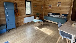 Ein gemütliches Blockhaus mit Holzvertäfelung, einem Bett, einem Esstisch und einer Gitarre.