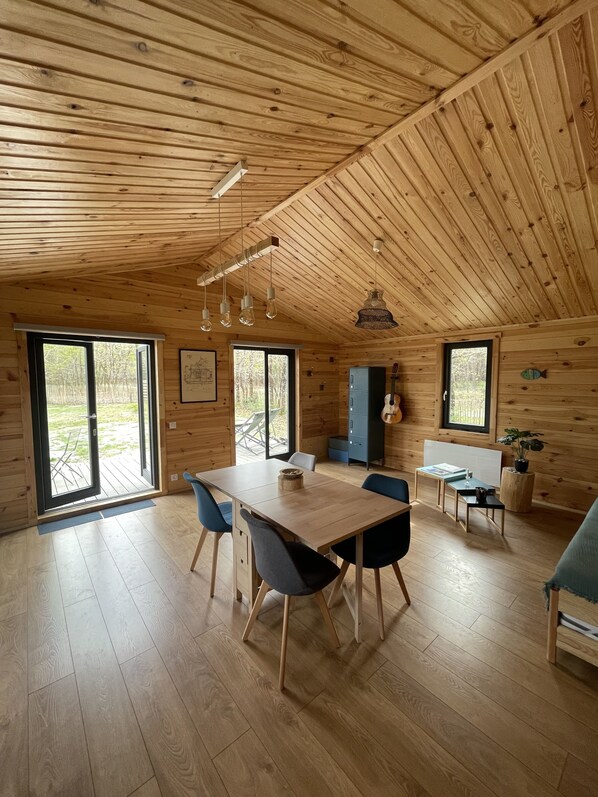 A spacious wooden cabin with a dining area, kitchen, and large windows.