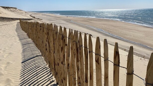 Ein sandiger Strand mit einer Holzumzäunung und freiem Blick auf das Meer.