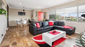 A modern living room with a black sectional sofa, a white coffee table, and a dining area with a table and chairs. - Beach Haven on The Hill (The Hill)