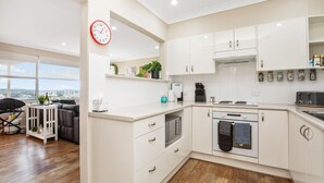 A modern kitchen with white cabinets, a built-in oven, and a coffee machine. There is a view of the city through large windows. - Beach Haven on The Hill (The Hill)