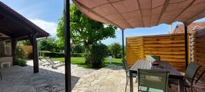 An outdoor patio with stone flooring, a wooden table with chairs, and a pergola with a canopy.