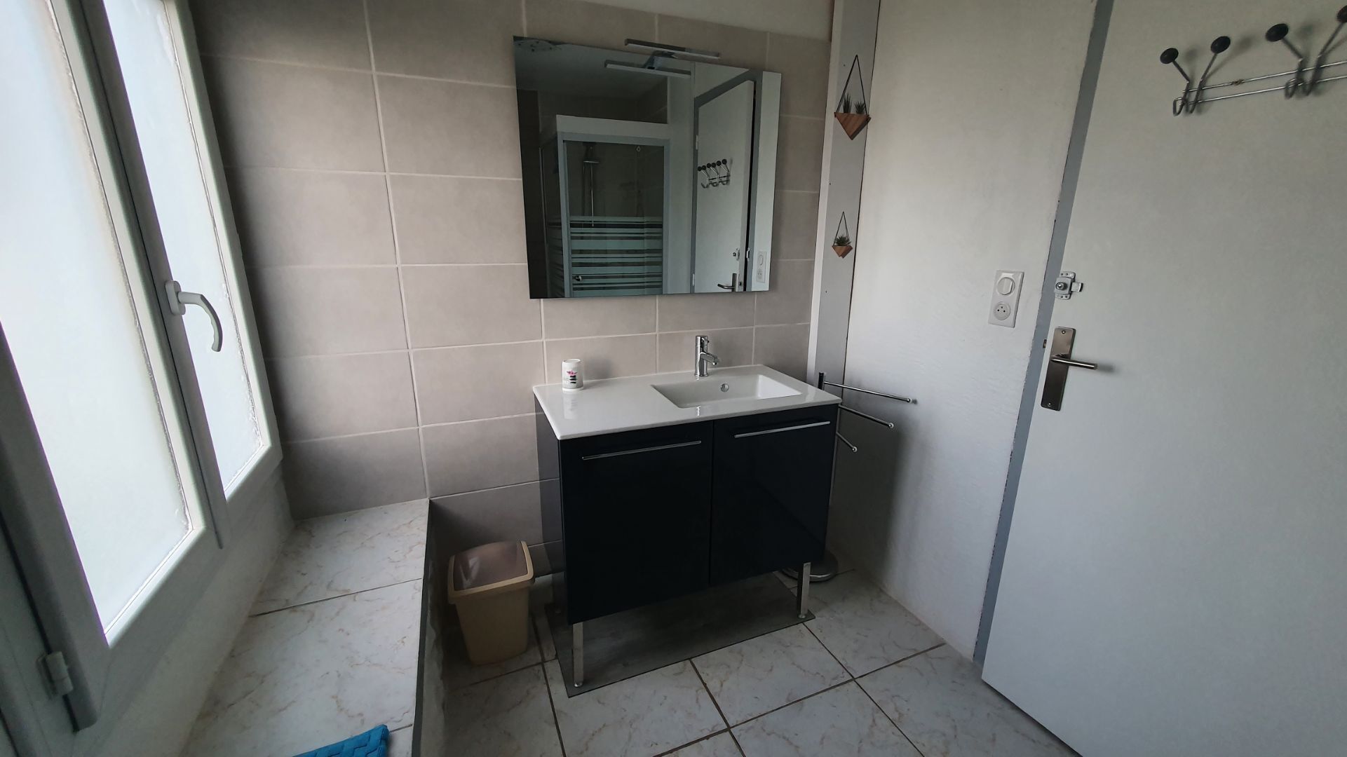 Een badkamer met een witte wastafel, donkere kastjes, een spiegel en een douche.