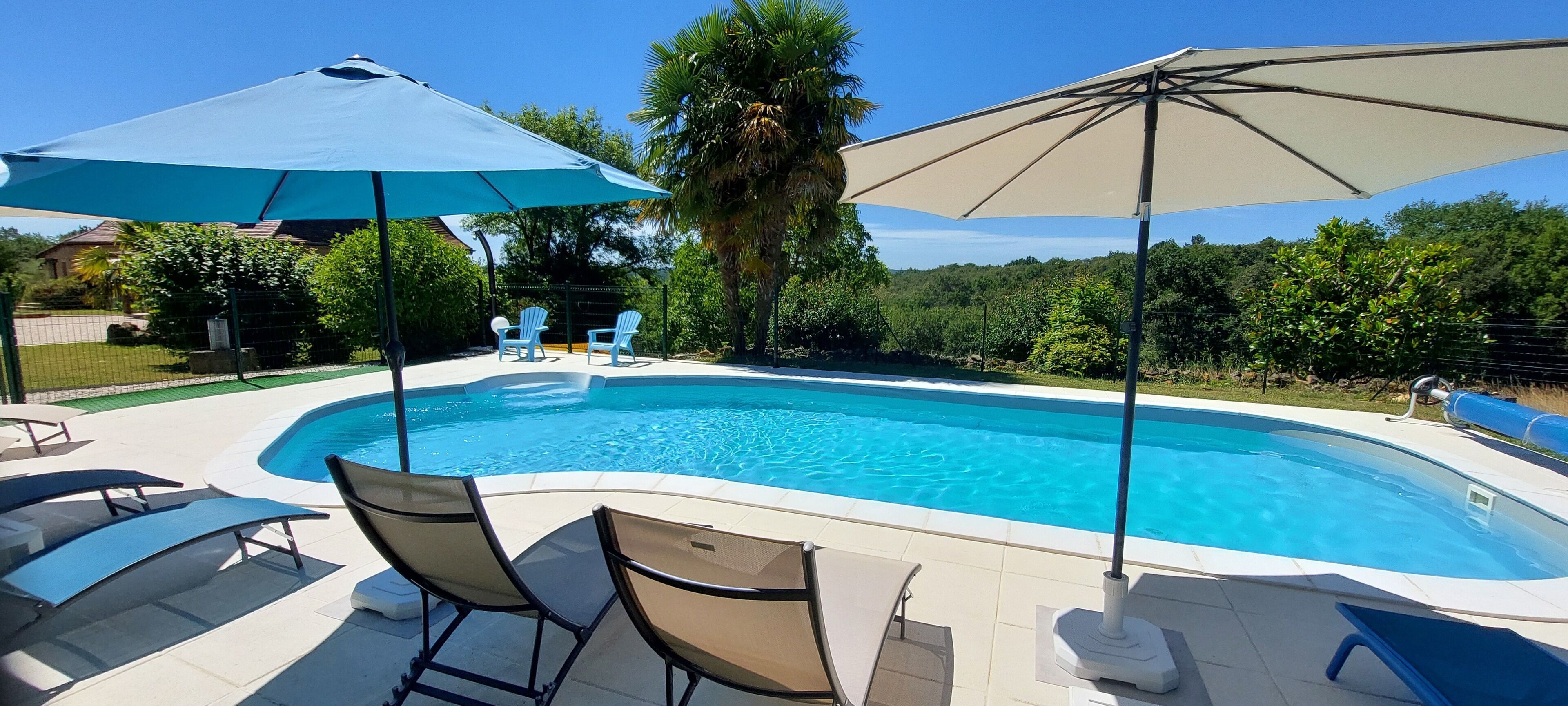 A swimming pool with lounge chairs and umbrellas, surrounded by greenery and a fence.