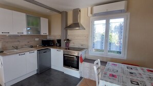 A compact kitchen with white cabinets, a microwave, a coffee maker, and an oven. There is a window with a view of greenery outside. - Le Bellevue, quiet gite with panoramic view 10 minutes from Sarlat (Vezac)