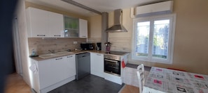A compact kitchen with white cabinets, a microwave, a coffee maker, and an oven. There is a window with a view of greenery outside. - Le Bellevue, quiet gite with panoramic view 10 minutes from Sarlat (Vezac)