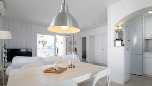 Uma sala de jantar moderna e minimalista, com mesa de madeira e cadeiras brancas, luminária pendente e vista para o exterior.