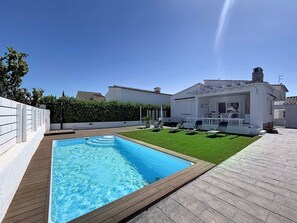 Ein Swimmingpool, eine Rasenfläche und ein weißes Haus mit einem Balkon.