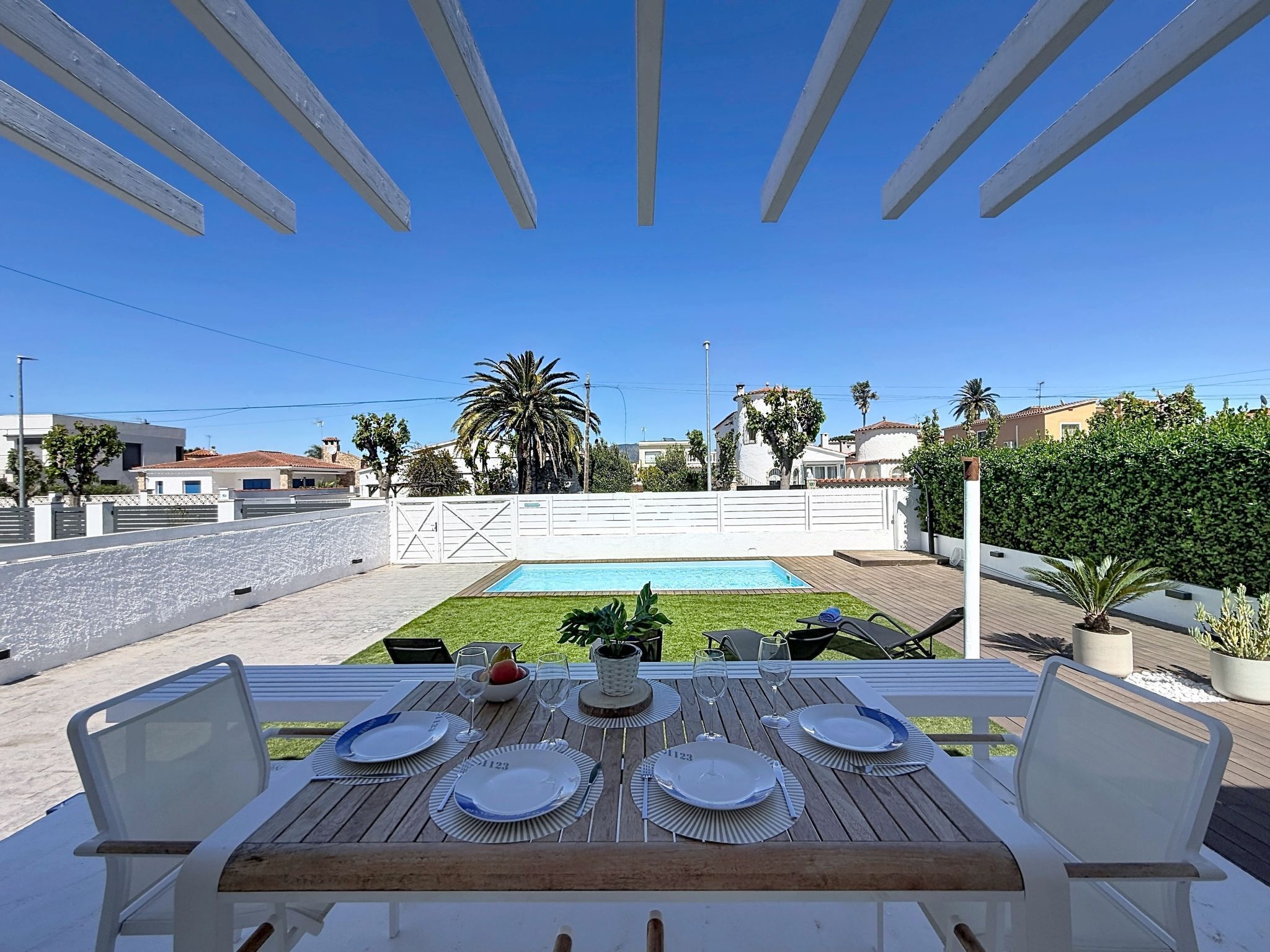 Un área de comedor al aire libre con piscina, sillas blancas y una mesa preparada para cuatro.