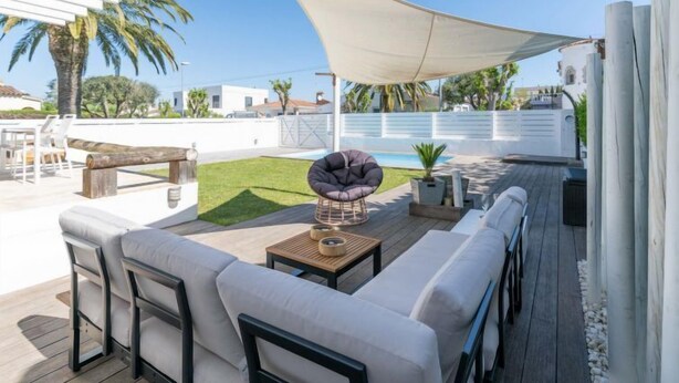 Um pátio externo com sofá, cadeiras, mesa e toldo de tecido.