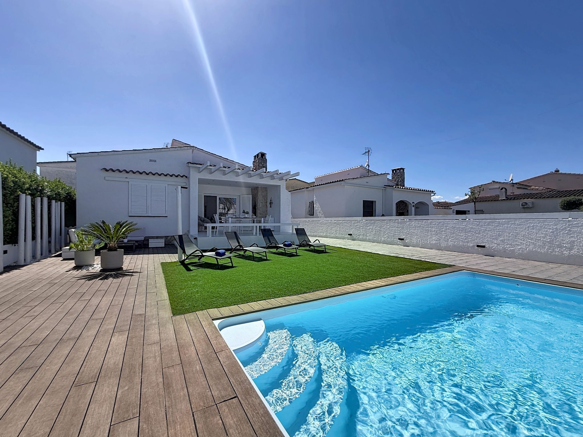 A poolside area with a wooden deck, a swimming pool, and a white building with a patio.