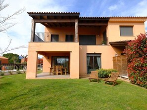 A two-story building with a balcony, a covered patio, and a well-maintained lawn.