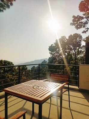 A wooden table and chair on a balcony with a view of trees and hills. - BluSalzz Escapade, Lansdowne - Uttarakhand (Lansdowne)