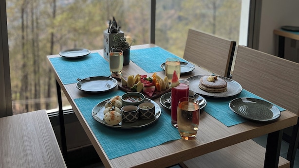 Mesa de comedor servida con platos, vasos y una vela, con vistas a un paisaje montañoso.