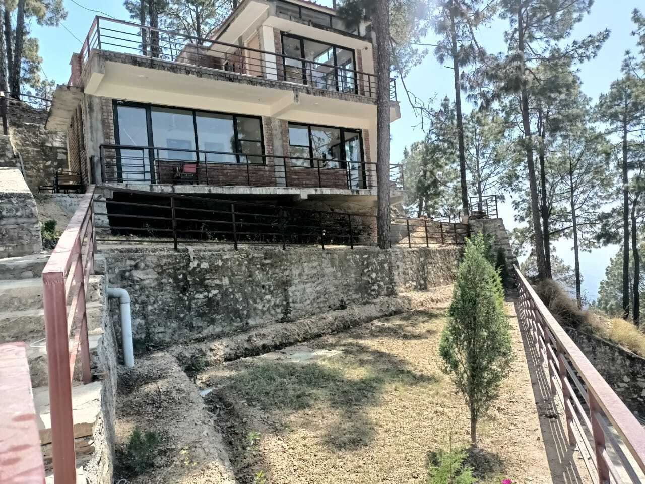 A two-story building with large windows and a balcony, surrounded by trees and a stone wall.
