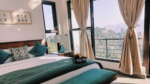 Habitación de hotel con una cama grande, una mesita de noche, una lámpara y vistas a las montañas.