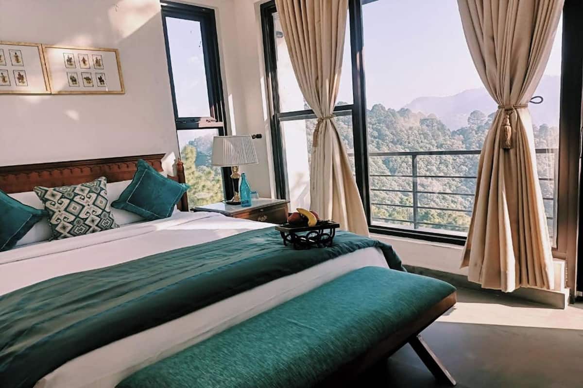 A hotel room with a large bed, a nightstand, a lamp, and a view of the mountains.