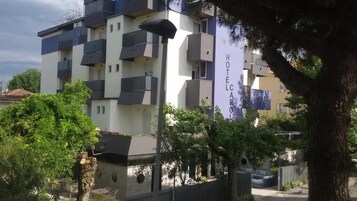 Un hotel de varios pisos con balcones, un letrero que dice "HOTEL CARLO" y follaje circundante.