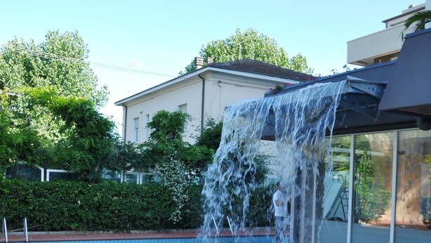 Une piscine agrémentée d’une cascade, entourée d’une terrasse carrelée et de verdure.