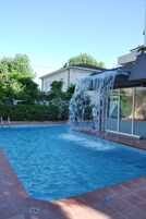 Una piscina con una cascada, rodeada de un solado alicatado y follaje.