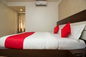 Habitació d'hotel amb un llit, un edredó vermell i blanc, i aire condicionat fixat al sostre.