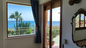 A room with a large window overlooking a coastal view, including palm trees and the sea. - Heart of Ognina - Veliero - Apartment with sea view (Ognina)