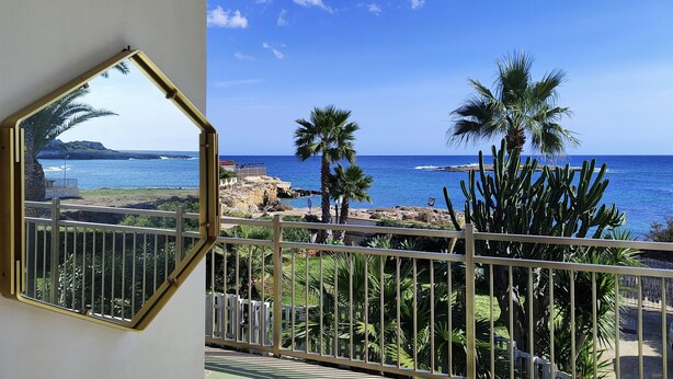 A balcony with a view of the ocean, palm trees, and rocky coastline. - Heart of Ognina - Veliero - Apartment with sea view (Ognina)