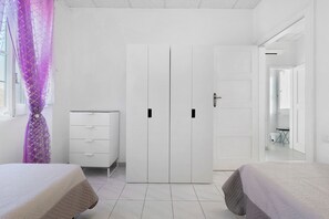 A bedroom with two beds, a white wardrobe, a dresser, and a bathroom visible through an open door.