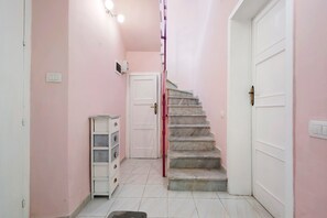 A hallway with a staircase leading to a door, a small cabinet, and a light switch on the wall. - Montello Sweet House Holiday Home in Cagliari – Central, Well-Connected, and Comfortable (Cagliari)