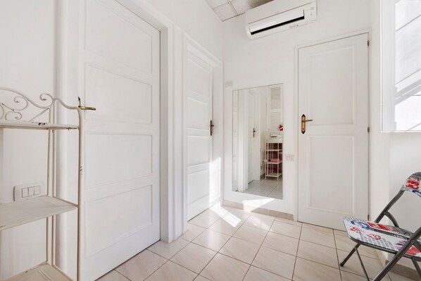 A hallway with white doors, a metal chair with a colorful pattern, and a tiled floor.