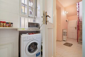 A compact laundry area with a washing machine, a microwave, and spice jars on a shelf. - Montello Sweet House Holiday Home in Cagliari – Central, Well-Connected, and Comfortable (Cagliari)
