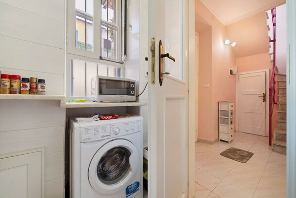 A compact laundry area with a washing machine, a microwave, and spice jars on a shelf.