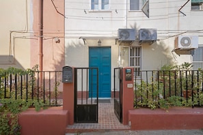 A building with a blue door, two air conditioning units, a metal gate, and a mailbox.